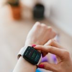 Anonymous female sitting on yoga mat on floor and looking at smart watch on hand