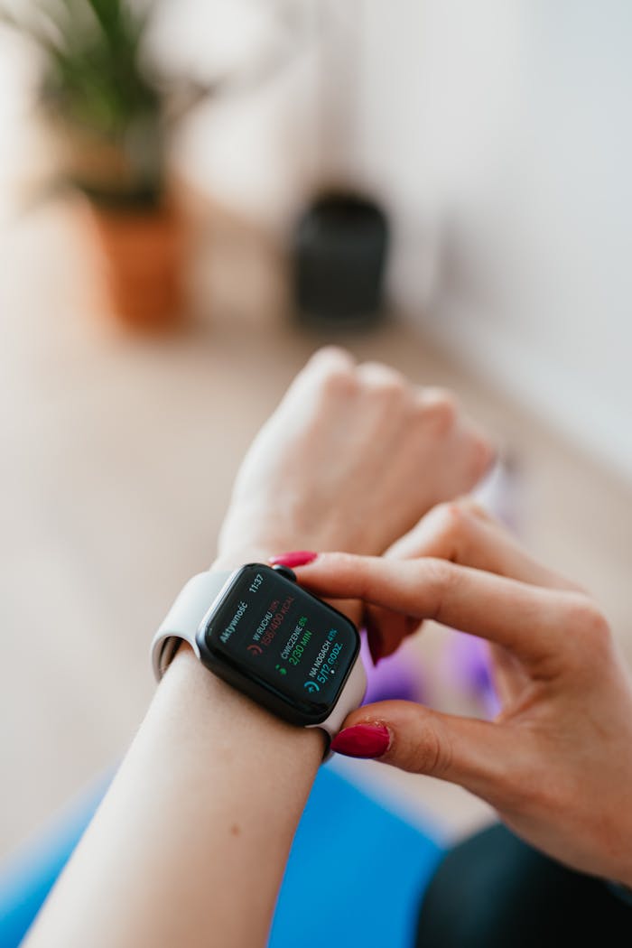 Anonymous female sitting on yoga mat on floor and looking at smart watch on hand